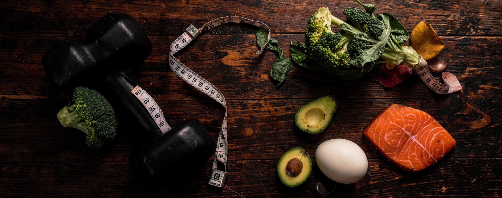 Dumbbell, measuring tape and fresh produce on a wooden table